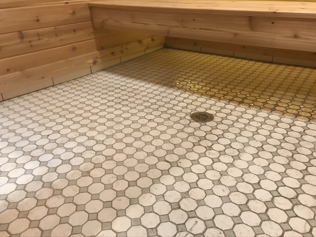 Tile floor, tile baseboard and center floor drain in sauna